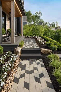 an outdoor walkway leading to a house with flowers in the foreground and landscaping on either side