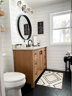 a white toilet sitting next to a wooden vanity in a bathroom under a mirror above a sink