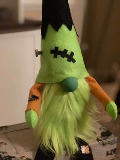 a green stuffed toy with black eyes and long hair sitting on top of a table