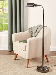 a living room with a chair, lamp and rug on the floor in front of a window