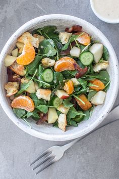 a salad with oranges, cucumbers and other vegetables in a white bowl