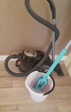 a bucket filled with water next to a vacuum and a duster on the floor