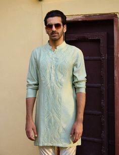 Introducing the raas bandi set, an elegant ensemble designed for men's haldi, mehndi, or sangeet occasions. This set features a mint green front-open nehru jacket and a matching mint green front-open kurta, creating a harmonious and refreshing look. Paired with an off-white churidar, this outfit combines contemporary style with traditional elements. The mint green nehru jacket is designed with a sleek front-open silhouette, perfect for layering. Its soft color is vibrant yet understated, adding a touch of sophistication to any festive event. The matching mint green kurta continues the seamless aesthetic, with its front-open design allowing for easy movement and breathability. The off-white churidar completes the set, providing a classic and comfortable contrast to the mint green tones. Thi Green Bollywood Bandhgala With Chikankari Embroidery, Pista Green Lawn Suit With Cutdana For Diwali, Pista Green Bandhgala With Dabka, Diwali Pista Green Lawn Suit With Cutdana, Green Straight Kurta Bandhgala With Dabka, Festive Pista Green Kurta With Cutdana, Green Bandhgala With Chikankari Embroidery For Eid, Green Bollywood Style Kurta, Bollywood Style Green Kurta