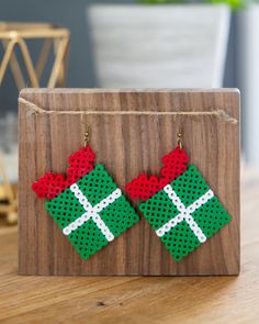 a pair of green and red christmas present shaped earrings on a wooden stand next to a potted plant