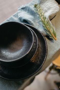 two black plates sitting on top of a table next to a napkin and pine branch