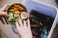 a person holding a green bowl filled with food next to a trash can on the ground