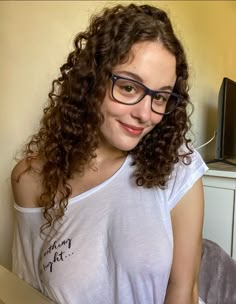 a young woman with glasses sitting on a bed in front of a tv and smiling at the camera