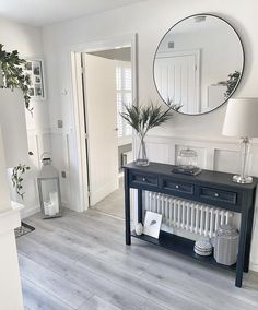 a living room with white walls and wood flooring, a large mirror on the wall