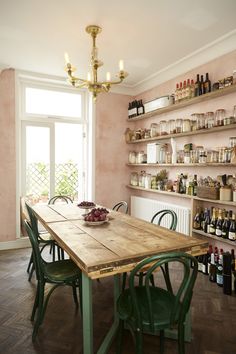 a dining room table surrounded by shelves filled with bottles and jars on the wall behind it