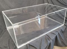 a clear plastic box sitting on top of a black cloth covered table next to a metal grate