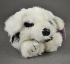 a white stuffed animal with black spots on it's face and paws, resting against a gray background