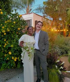 a man and woman standing next to each other in front of lemon trees with lights on them