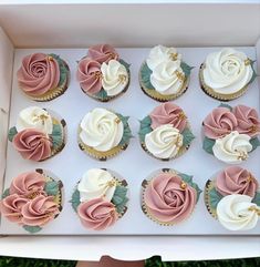 twelve cupcakes with pink and white frosting roses in a box on the grass