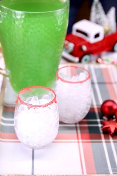 two glasses filled with green liquid sitting on top of a plaid table cloth next to christmas decorations