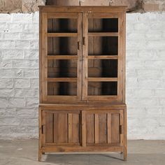 an old wooden cabinet with glass doors in front of a white brick wall and floor