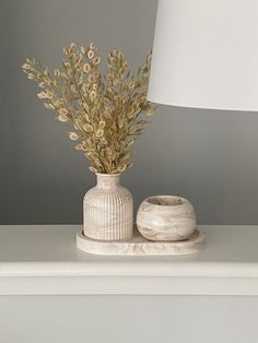 a white vase sitting on top of a table next to a lamp and a candle holder