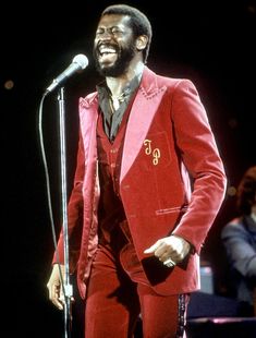 a man in a red suit standing next to a microphone and singing into a microphone