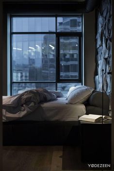 an unmade bed in front of a large window