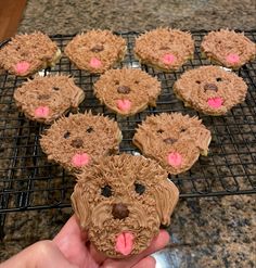 a person holding up a cookie with frosting on it in front of some cupcakes