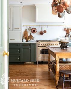 a kitchen with green cabinets and wooden floors, pots hanging from the ceiling over the stove