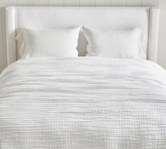 a white bed with two pillows on top of it and a headboard in the background