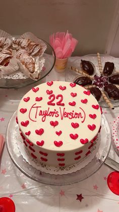 a white cake with red hearts on it sitting on a table next to other desserts