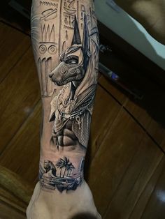 a man's arm with an egyptian tattoo on it and a dog in the background