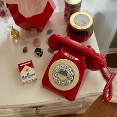 an old fashioned red phone sitting on top of a table next to some jars and other items