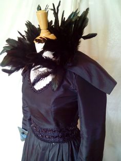 a black dress with feathers on it and a hat on top of the mannequin's head