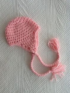 a crocheted pink hat laying on top of a white blanket next to a pair of scissors