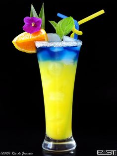 a tall glass filled with an orange, blue and yellow drink next to a purple flower