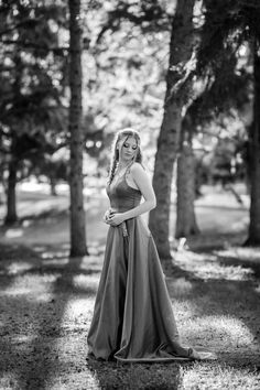 a woman in a long dress standing by some trees