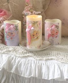 three candles are sitting on a table next to a lace doily and pink flowers