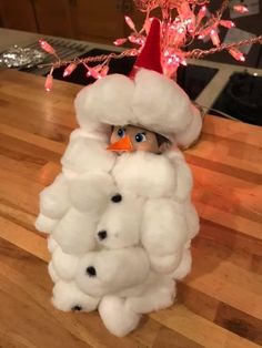 a stuffed animal wearing a santa claus hat and coat on a table with christmas lights in the background