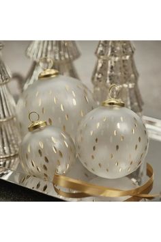 three white glass ornaments sitting on top of a table next to silver christmas tree decorations