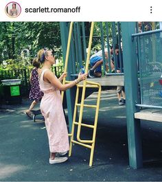 a woman climbing up the side of a yellow ladder at a play ground with children playing in the background