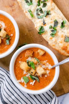 two bowls of tomato soup with bread on the side