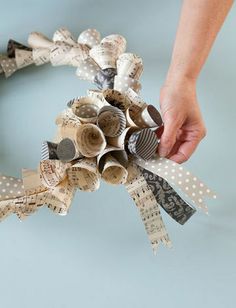 a person is holding up some old newspaper strips to make a wreath with ribbon and buttons