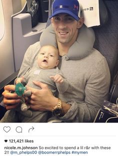 a man holding a baby wearing a baseball cap on top of his head and sitting in an airplane