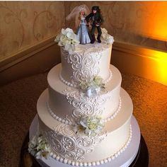 a wedding cake with white flowers on top and two figurines sitting on top