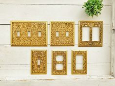 four decorative gold metal switch plates on a white wooden wall next to a potted plant