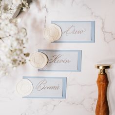 two name tags on a marble surface next to a wooden stamper and some flowers