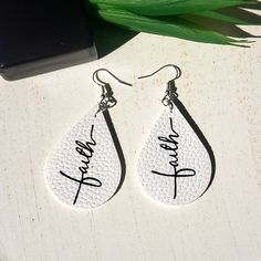 two white tear shaped earrings with the word faith written in cursive writing on them