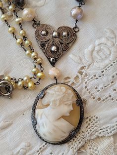 "My inspiration for this design was a beautiful antique shell cameo with a silver frame.  I left the pin on the back to not alter the antique value.  I hung her from a silver filigree heart and added a pearl chain and a couple of French bracelet pieces.    You will love her.   The length is 18 1/2\", You can hook the clasp on the pearl chain to change the length.   The cameo is 1 1/4\" long and  1 1/8\" wide." Vintage Cameo Necklace In Antique Gold, Lady Cameo Necklace, French Bracelet, Ornate Antique Gold Cameo Necklace, Antiques Value, Collectible Cameo Pendant Necklace, Ornate Cameo Necklace Collectible, Filigree Heart, Vintage Assemblage