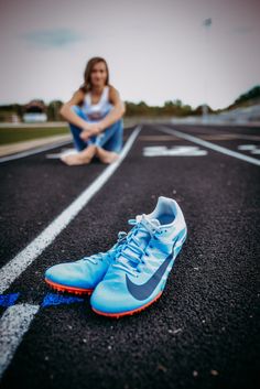 a woman sitting on the ground next to a pair of blue nike shoes with her legs crossed