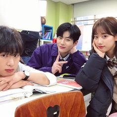 three young people sitting at a desk in front of books and laptops with their hands on their chins