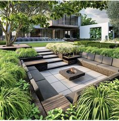 an outdoor fire pit surrounded by greenery and trees in front of a modern house