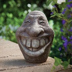 a statue of a laughing face sitting on top of a stone wall next to flowers