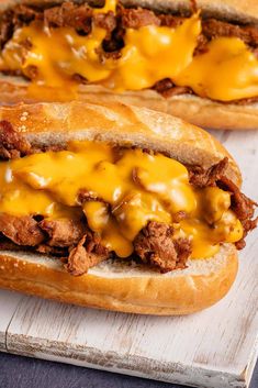 two sandwiches with meat and cheese sitting on a cutting board