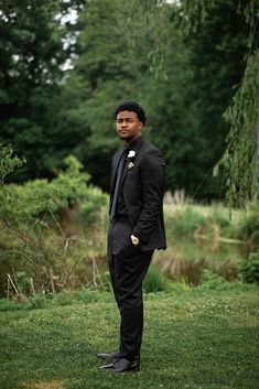 a man in a tuxedo standing on the grass with trees in the background